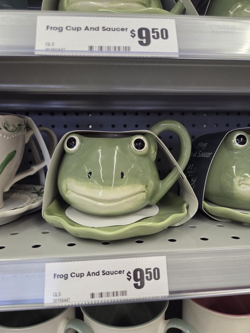 Photo of a green ceramic frog-shaped teacup and saucer on a store shelf, priced at $9.50 each with labels reading 'Frog Cup And Saucer'.