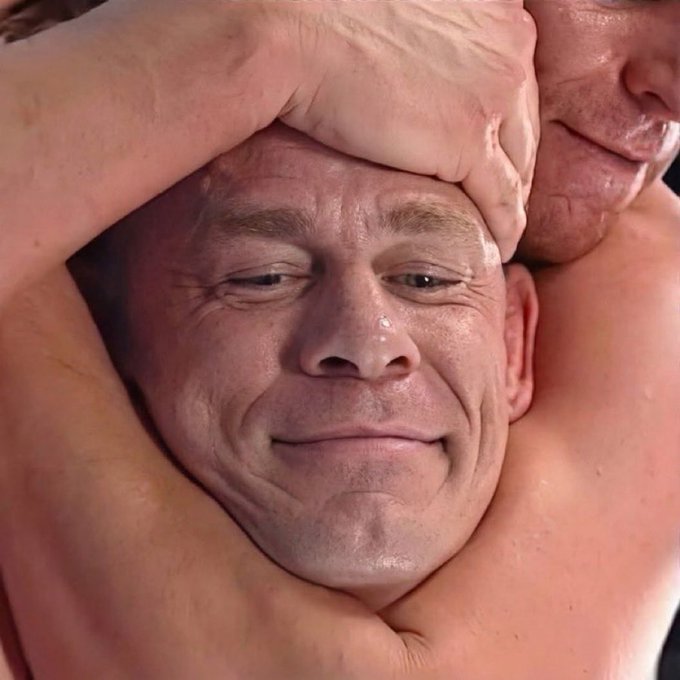 A close-up of a man with a flushed face and a strained smile, with his arm wrapped around his head.