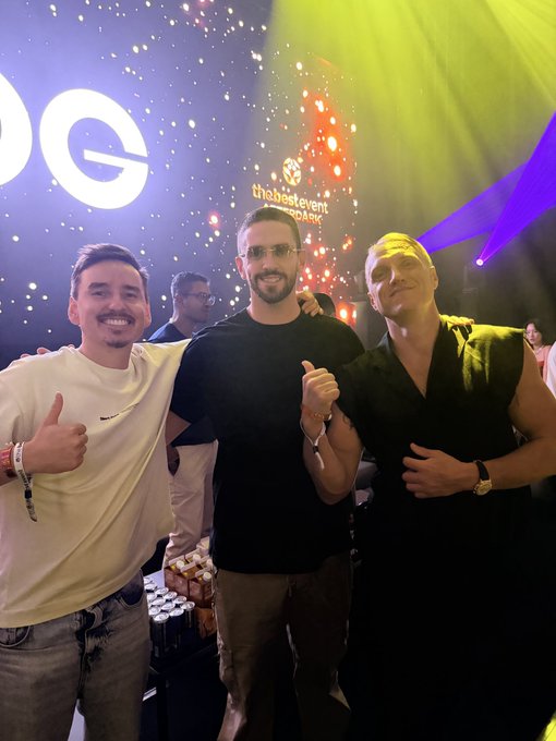 Three smiling men pose together at a nightclub event, with visible signage reading "the best event agency" in the background, while the caption confirms a fan-meeting moment with crypto personalities @MMCrypto and @carlmoon.