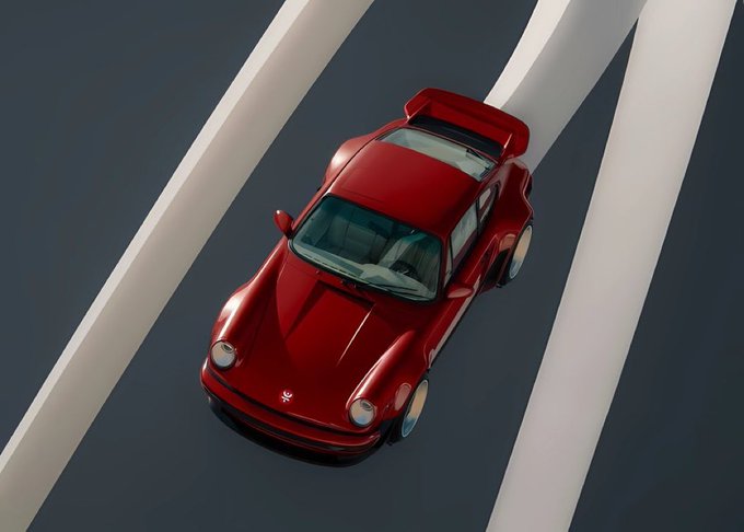 An aerial view of a dark red Porsche 911 with a rear spoiler driving on a gray road with white lane markings.