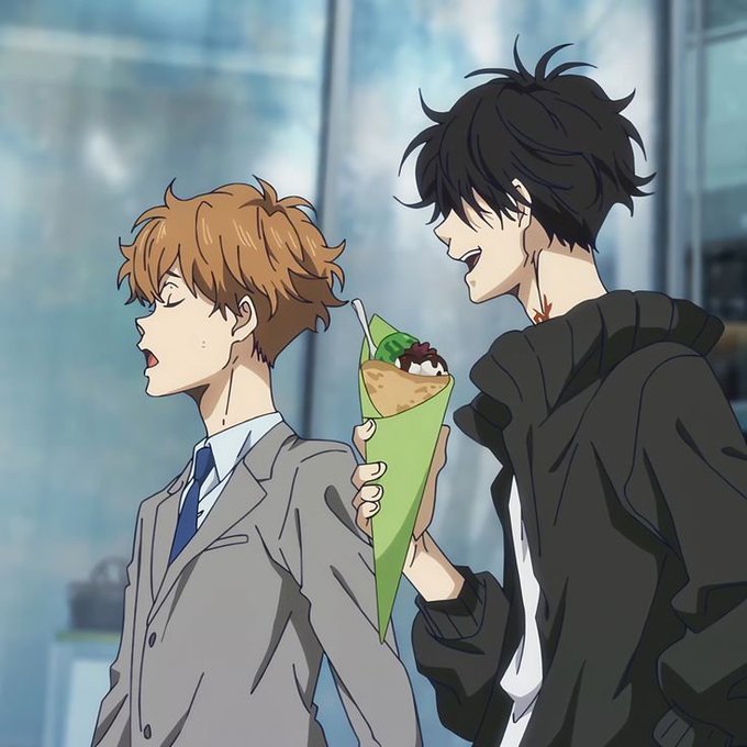 An anime illustration showing two young men in modern attire; one with orange hair in a gray suit looks surprised, while the other with black hair in a dark jacket holds a crepe wrapped in green paper.