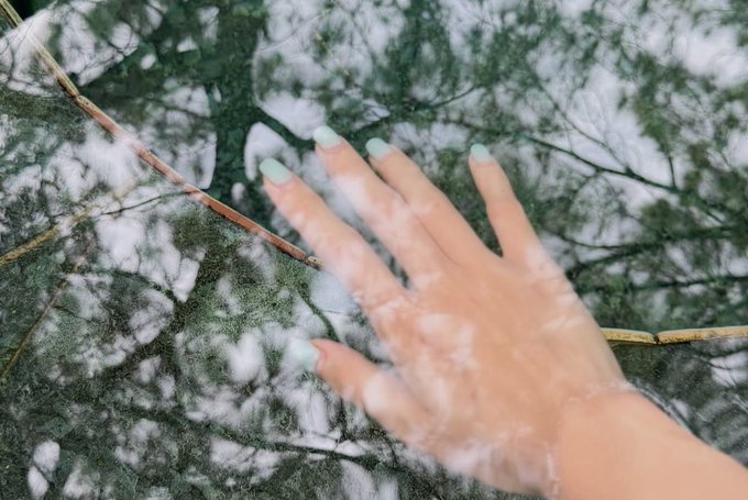 The image features a person's hand with green fingernails, reaching out towards a tree branch that has leaves hanging down from it. The background of the photo is blurred, drawing attention to the hand and its interaction with nature. The caption "gm good morning any plans for the weekend? i think it’s time for me to touch some grass @NomismaNetwork @useTria". This suggests a connection between the person's desire to connect with nature through touching leaves on the tree branch, and their intention to engage in outdoor activities or spend time outdoors during the weekend.