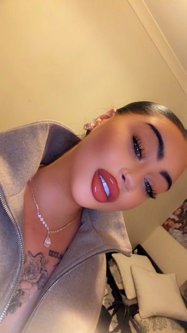 A close-up selfie shows a woman with dramatic makeup, glossy red lips, and a diamond pendant necklace, with a tattoo partially visible on her chest.
