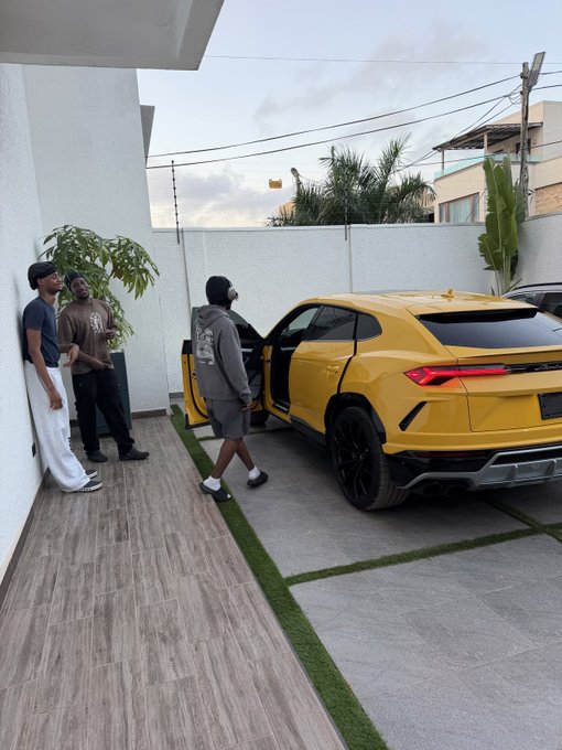 Three people standing outside near a yellow Lamborghini Urus SUV parked in a driveway.