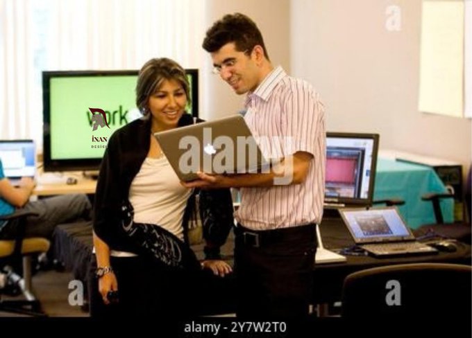 Two colleagues—a woman in a black cardigan and a man in a pink striped shirt—collaborate while looking at a laptop in what appears to be an office or computer lab setting, with monitors visible in the background. The image illustrates the caption's reference to the 2009 Facebook Fund award and early tech venture work, capturing the era of budding startup development before blockchain's mainstream rise.