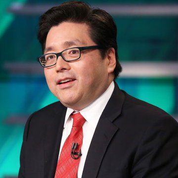 A professional photo of an East Asian man wearing black-rimmed glasses, a dark suit, white shirt, and red tie, speaking in what appears to be a television studio setting with a teal background.