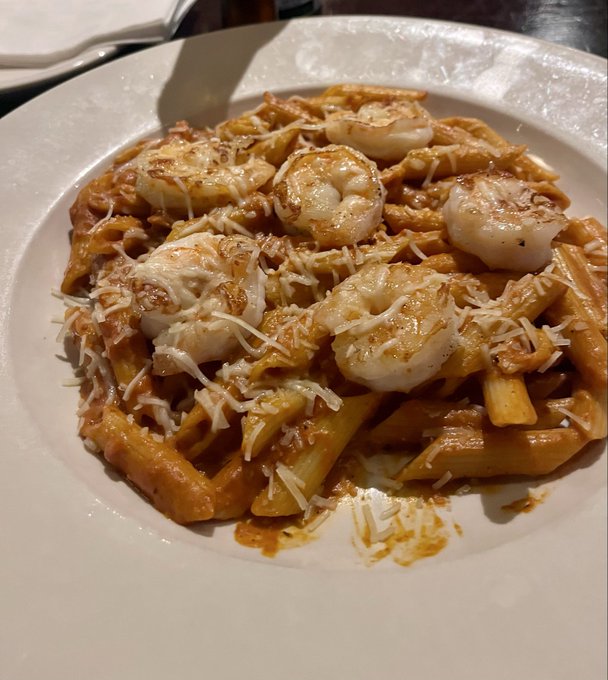 The image shows a plate of pasta covered in white sauce, shrimp, and cheese. There are at least six pieces of shrimp visible on top of the pasta. The dish appears to be a simple yet delicious meal that could be enjoyed by those who appreciate seafood flavors.