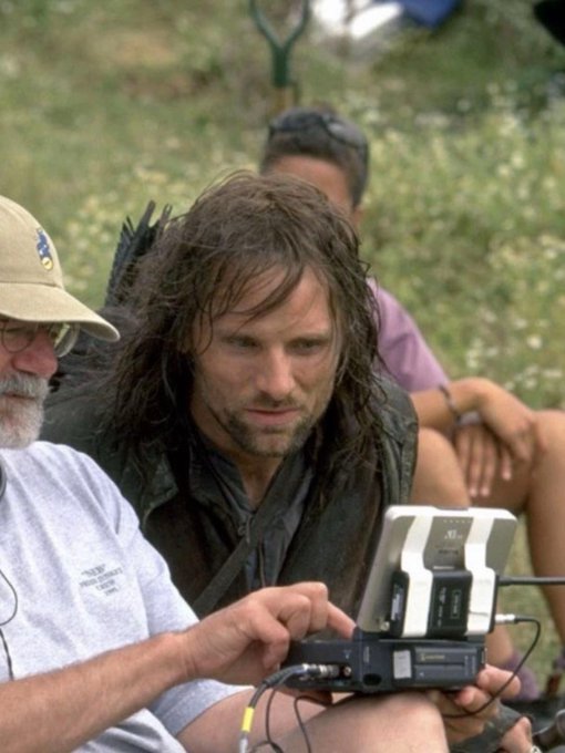 A behind-the-scenes photo showing actor Viggo Mortensen, who played Aragorn, on a film set while a crew member monitors a camera monitor.