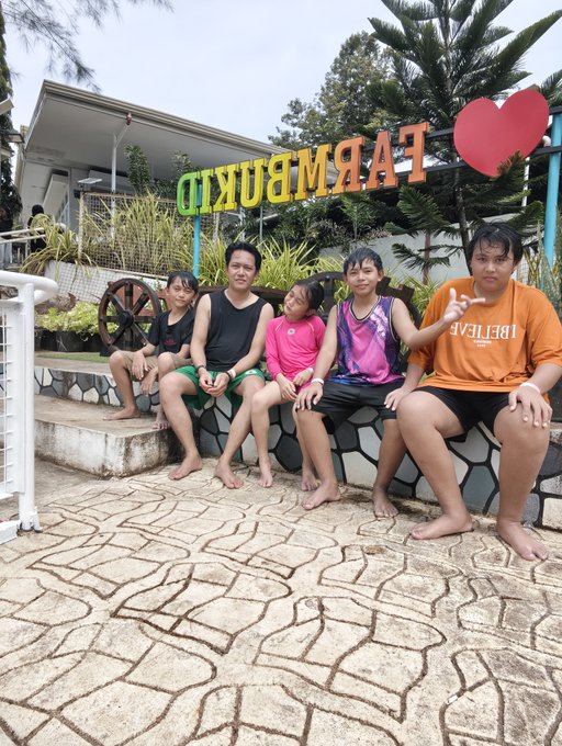 A group of five people sit on a stone ledge under a sign reading 'FARM BURITO' with a red heart symbol, posing together at what appears to be a tourist destination.