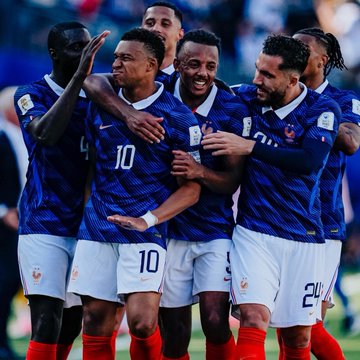 Several France national football team players, wearing blue jerseys with numbers 10 and 24 visible, embrace in celebration on the pitch. The image captures the squad's camaraderie, visually reinforcing Polymarket's projection of France as a 59% favorite to reach the 2026 World Cup final.