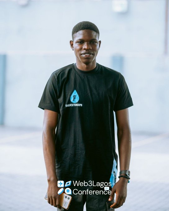 A young man wearing a black 'Faucetdrops' t-shirt poses at the Web3Lagos Conference, holding a phone with the event's branding visible at the bottom of the image.