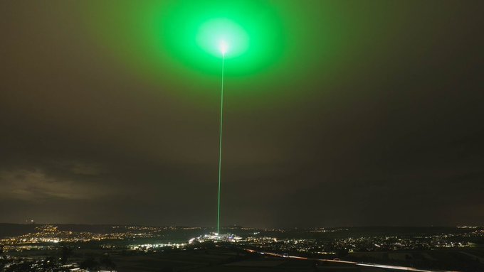 A green laser beam shoots dramatically into the night sky above a cityscape, symbolizing the bullish "UPtober" sentiment as Bitcoin approaches $86K, Ethereum hits $2,750, and Solana reaches $122 for life-changing crypto gains.