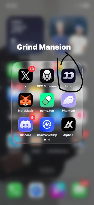 iPhone home screen screenshot labeled "Grind Mansion" showing a folder of crypto/finance apps including X (with 13 notifications), DEX Screener, fomo (circled in black), MetaMask, pump.fun, Phantom, Discord, CoinMarketCap, and AlphaX.