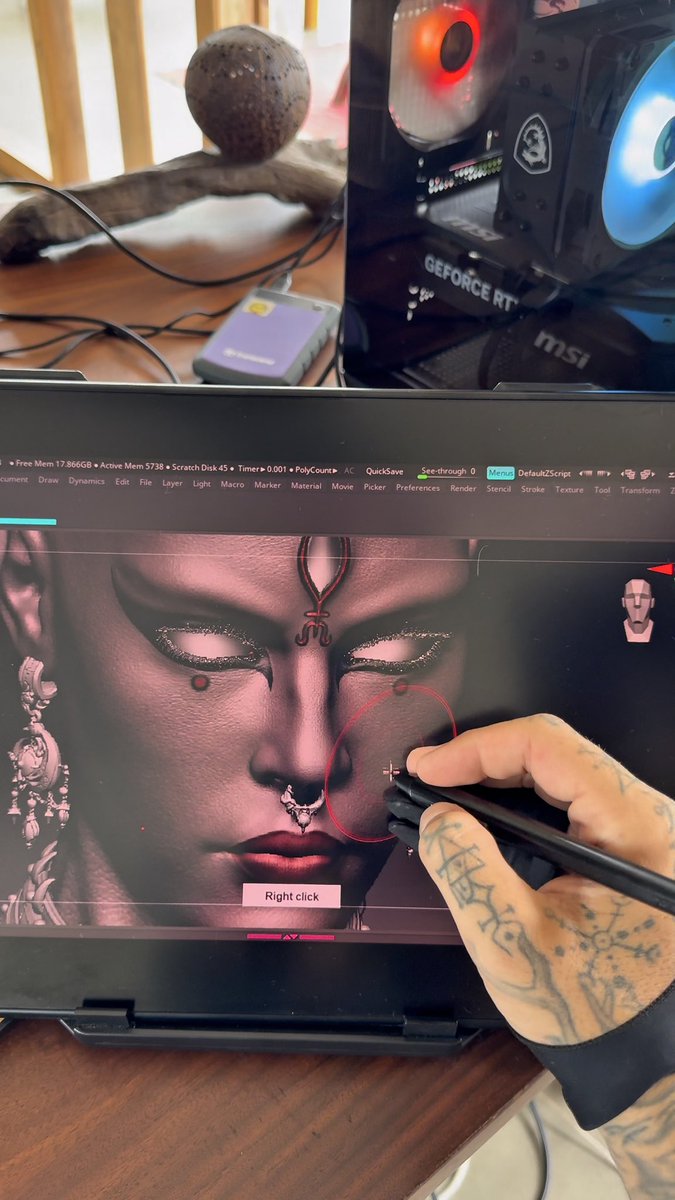 A tattooed hand uses a stylus on a laptop running 3D modeling software (ZBrush), sculpting a detailed face with ornate jewelry, with an MSI GeForce RTX gaming PC visible in the background.