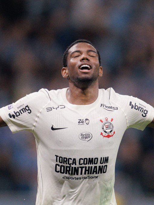 A soccer player in a white Corinthians jersey emblazoned with "TORÇA COMO UM CORINTHIANO" and sponsors like "bmg" and "Frimesa" celebrates with eyes closed and mouth open in apparent jubilation, likely responding to criticism of his effort by passionately demonstrating his dedication to the club.