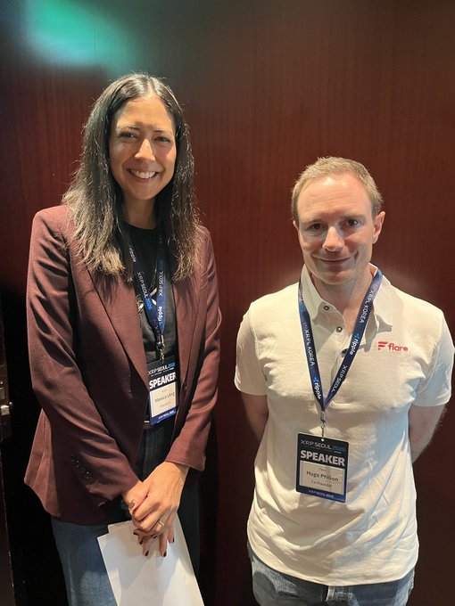 A man and a woman posing together, both wearing lanyards with speaker badges at an event.
