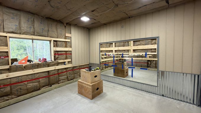 An unfinished room with exposed insulation, metal wall panels, a mirror, and plyometric boxes, suggesting a home gym under construction.