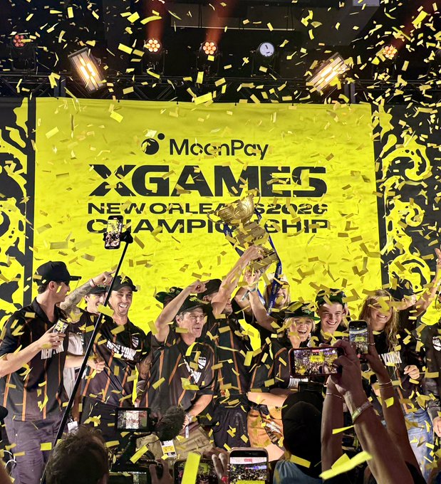 A team celebrates on stage while holding a trophy under a shower of yellow confetti, with a banner reading "MoonPay X GAMES NEW ORLEANS 2026 CHAMPIONSHIP" visible behind them. The image captures the championship victory moment that the social media giveaway post is celebrating, showcasing Team New York as the winners of the MoonPay X Games League Championship.