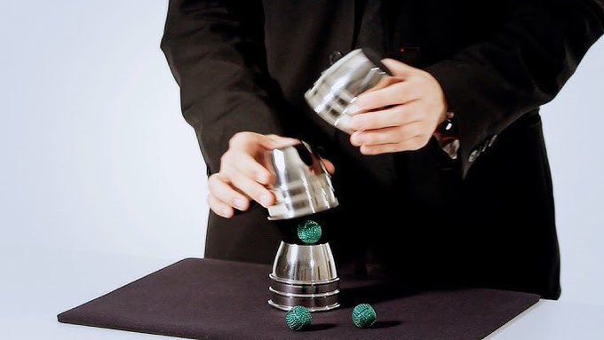 A magician performs a cups and balls trick, mirroring the strategic financial maneuvers described in the accompanying post. The image symbolizes the complex and often deceptive nature of financial transactions.