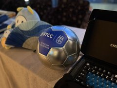 A plush soccer ball featuring "BTCC" branding sits next to an "exc" laptop, cleverly tying into the post's joke about being "busted" sneaking in references to BTCC (a crypto exchange) at work before heading off to the office.