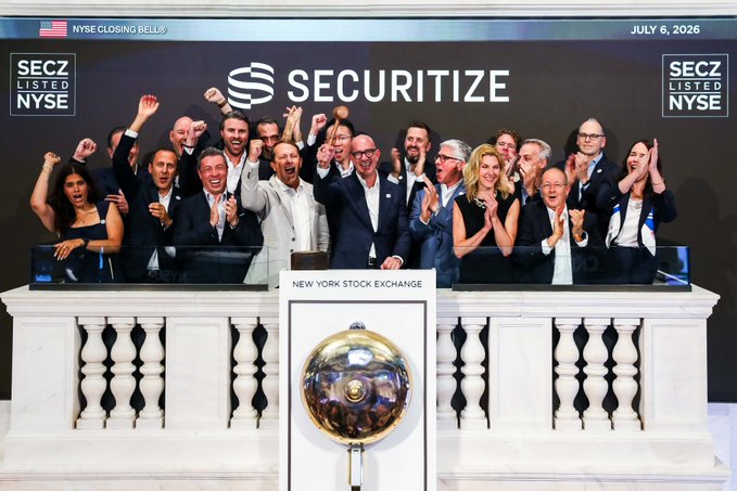 The image captures a celebratory moment at the New York Stock Exchange on July 6, 2026, where the SECURITIZE team and guests cheer from the balcony after ringing the NYSE Closing Bell, marking a milestone event for the company. The banner behind them highlights "SECURITIZE," "NYSE CLOSING BELL," and "SEC LISTED NYSE," reinforcing the significance of this recognition on the exchange's iconic podium.