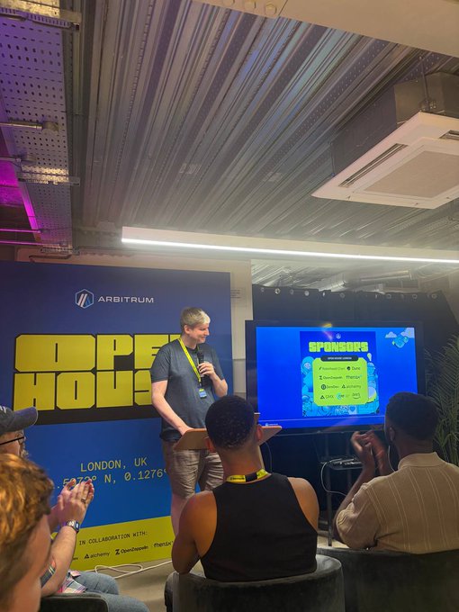 A man speaks into a microphone at a podium during an Arbitrum "Founder House" event in London, with a screen displaying sponsor logos (including Pyth and Zircuit) behind him. The setup reflects the post's announcement of three days of building, shipping, and connecting within the Arbitrum ecosystem.