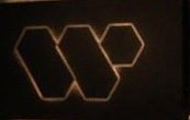 The image features a logo with a hexagon shape and the letters "W" and "P" inside of it. The background appears to be black, but there are some lights shining through, making the logo stand out more prominently against the dark backdrop.