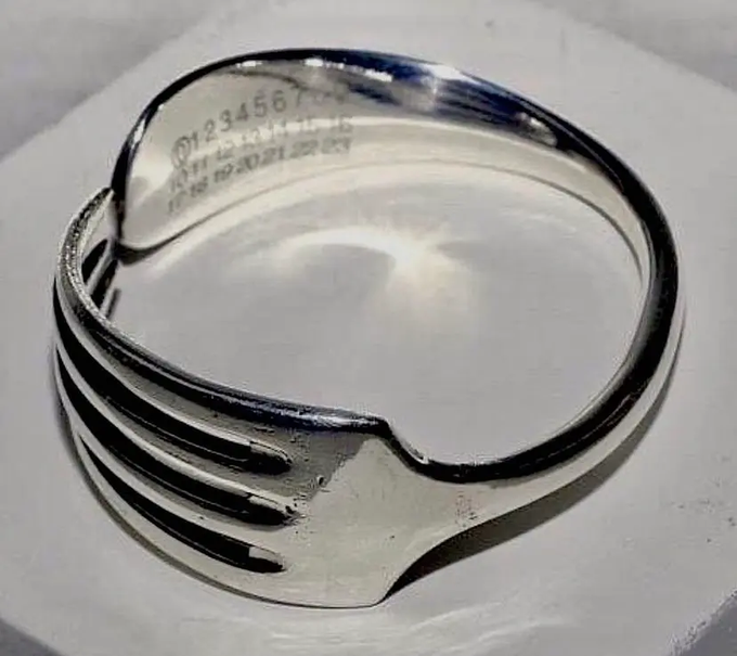 A polished silver ring or metallic object with engraved numbers and text sits on a light surface.