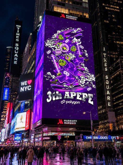The image shows a large billboard advertisement for 3JAPPE, which stands out against the backdrop of Times Square New York City at night. The billboard features a cartoon skier with purple hair and white pants, surrounded by various objects such as a snowboard, ski poles, and a pair of skis. The scene is illuminated by bright lights, creating an eye-catching display that captures the attention of passersby in the busy city environment.