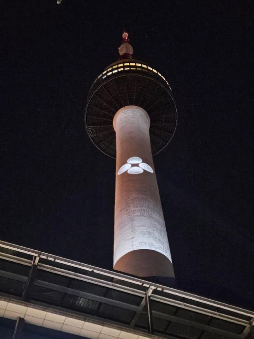 A nighttime view of Seoul's illuminated Namsan Tower displaying the Doppler Finance logo projected onto its facade, with the caption noting the surprise of seeing the @doppler_fi branding showcased on the iconic landmark.