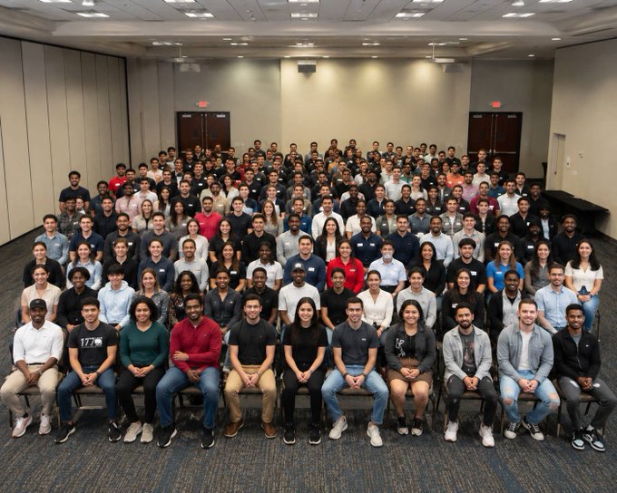 A large group photo of diverse people posed in rows in what appears to be a conference room or event hall.