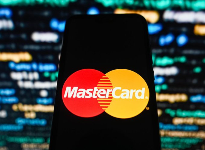 The image features a black smartphone with the Mastercard logo displayed prominently on its screen, indicating that the company has recently launched an AI-powered feature for Bitcoin transactions. The text "Just In" suggests that this information was shared as part of a recent announcement or update related to Mastercard's involvement in cryptocurrency transactions.!