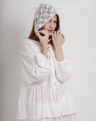 A woman wearing a white dress and an aluminum foil hat, standing against a plain white wall.