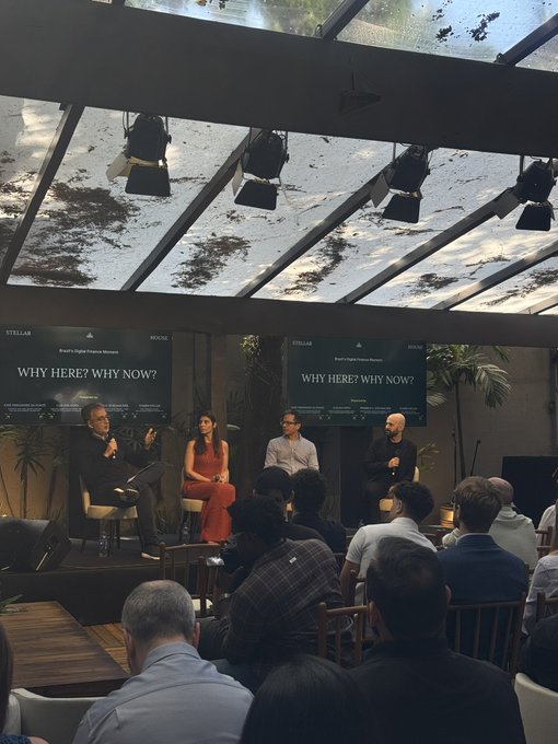 Four panelists sit on a stage for a 'Stellar x Polygon Partners Malaysia' event titled 'WHY HERE? WHY NOW?' held at RÜCÜS. An audience watches from the foreground beneath a glass ceiling dotted with stage lights.