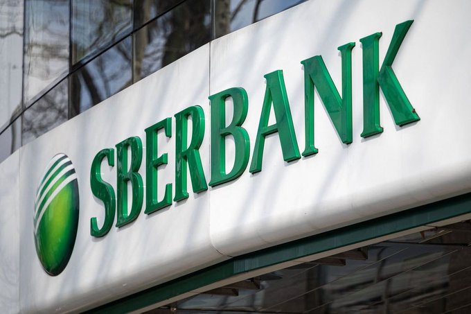 The image shows a green and white Sberbank sign mounted on the exterior of a building, featuring the bank's logo and name in bold lettering, representing Russia's largest financial institution that is set to introduce Bitcoin-collateralized loans under new digital asset legislation.