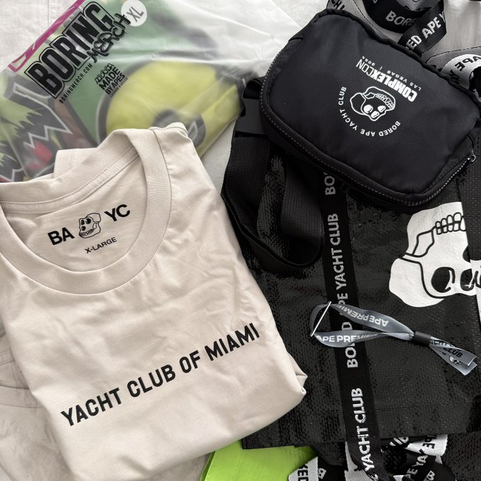 A streetwear flat lay featuring a BAPE 'BORING' XL shirt, a cream 'YACHT CLUB OF MIAMI' t-shirt with skull logo, a BAPE crossbody bag, and matching lanyards.