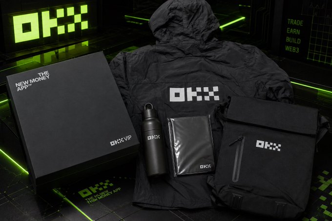 A promotional product photo displays black OKX-branded merchandise including a VIP box, hooded jacket, water bottle, sealed pouch, and bag, arranged on a dark surface with green neon 'OKX' signage reading 'THE NEW MONEY APP' and 'TRADE EARN BUILD WEB3'.