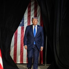 Donald Trump emerges from behind curtains with an American flag backdrop, visually accompanying the announcement that U.S. government documents will replace the term "artificial intelligence" with "super intelligence."