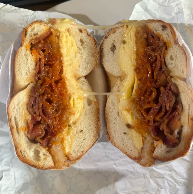 A close-up of a breakfast sandwich cut in half, revealing bacon, scrambled eggs, and melted cheese on a bagel.