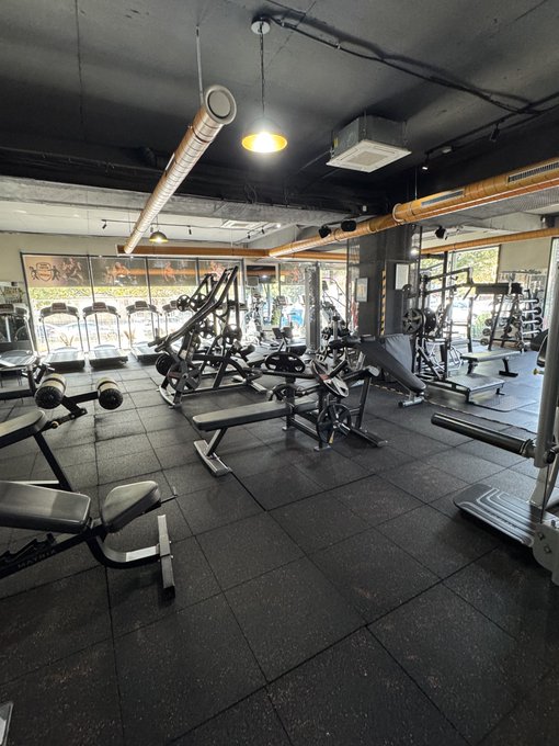 An interior view of a gym equipped with treadmills, weight benches, and other fitness equipment under industrial-style ceilings.