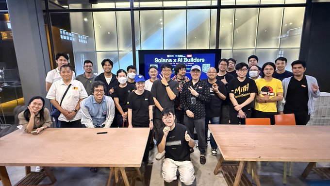 A group photo of approximately 20 people posing at a 'Solana x AI Builders' event, with a man in the front kneeling.
