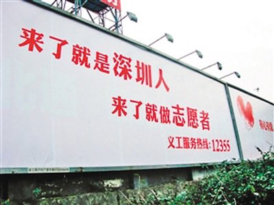 A billboard with red Chinese text reading '来了就是深圳人 来了就做志愿者' and a service hotline '12355' below.