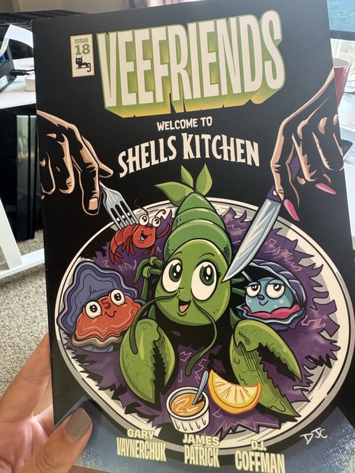 A hand holds a copy of VEEFRIENDS Issue 18 comic book titled "Welcome to Shell's Kitchen," featuring cartoon seafood characters on a plate and listing creators Gary Vaynerchuk, James Patrick, and DJ Coffman.