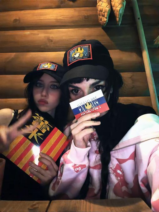Two women pose for a selfie wearing black "MILADY MAKER" branded trucker hats, with one holding a card reading "MILADY" and "BUY MILADY," while the other displays an item with "MILADY" text on a red and yellow striped background. The image appears to serve as meme-style "evidence" supporting the post's call to defend the Milady Maker NFT brand and "gaykeep" culture from perceived disrespect.