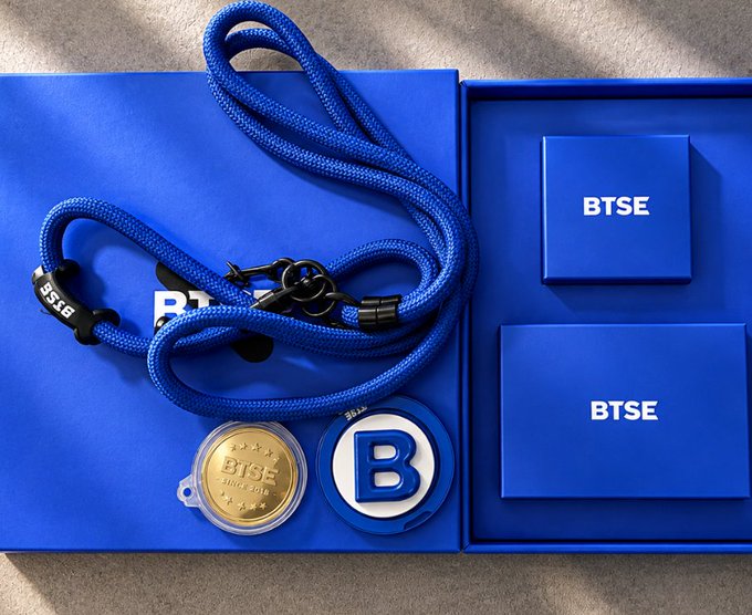 A blue BTSE branded gift box containing a blue lanyard, a gold BTSE coin, and a BTSE lapel pin in its packaging.
