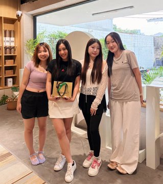Four women pose together indoors; the second from the left wears a black "TEAM CHIEFS" t-shirt and holds a green football-shaped balloon, while the others wear casual tops and bottoms.