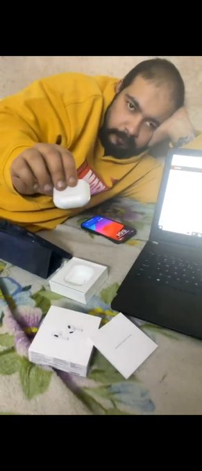 A man in a yellow hoodie holds up an AirPods case while unboxing new wireless earbuds, surrounded by product packaging on a carpet next to a laptop and phone. The image contrasts his newfound material success with the post's message about transforming from a "panda" to a "bull," suggesting his crypto gains funded these lifestyle upgrades.