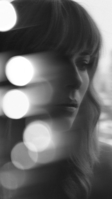 A contemplative black and white portrait of a woman with long hair, her face partially illuminated amid soft, glowing bokeh lights, capturing a quiet moment between illumination and shadow.
