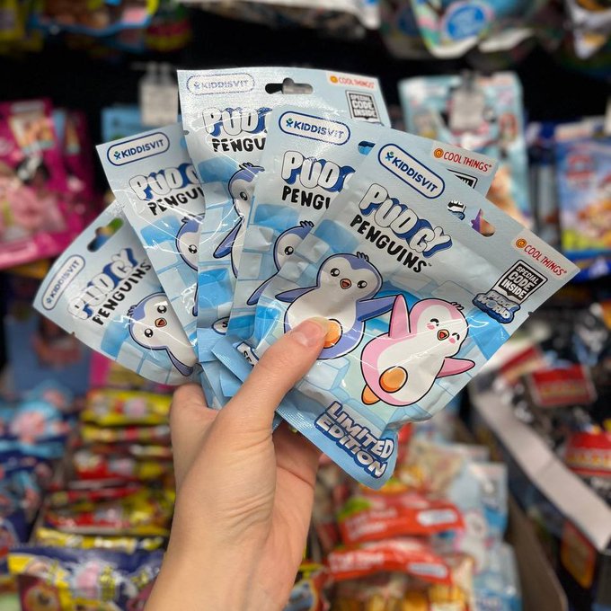 A hand holds up four 'POO & PENGUINS' limited edition Kiddisvit candy packets in a store aisle.