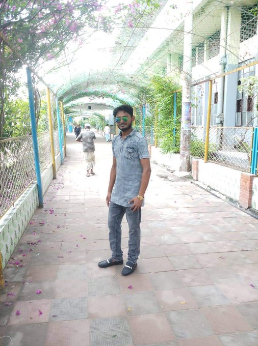 A young man in sunglasses and a denim shirt stands on a tiled walkway beneath a flowering archway, smiling faintly at the camera. The image humorously mirrors the caption's mood of vague anticipation—posing with quiet confidence despite the "no one knows" uncertainty of when sleep (or the CT launch) will actually arrive.